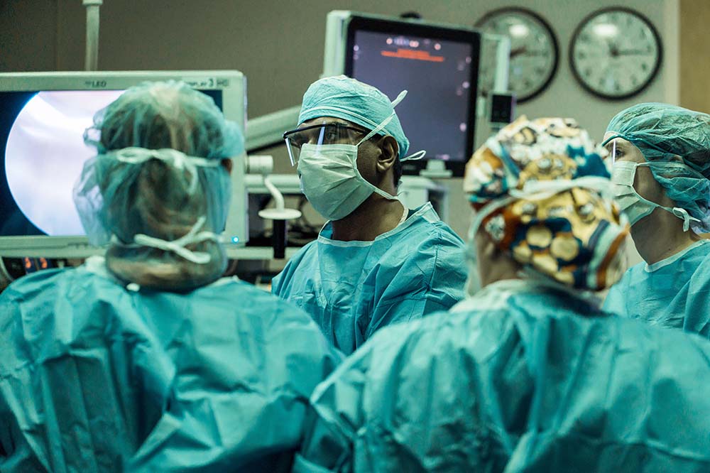 People in surgical scrubs gather in a group with clocks and monitors behind them.