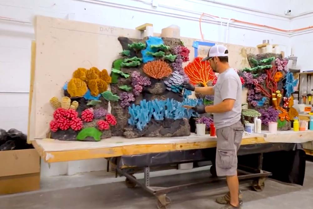 Man stands in front of a table holding colorful coral that will be installed in an aquarium.