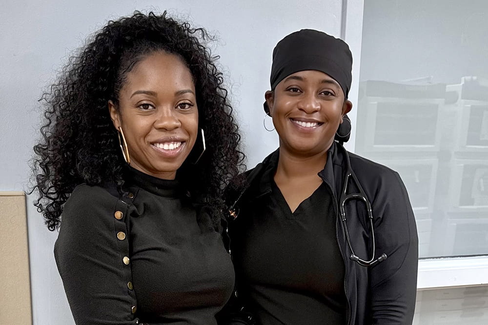 Two women wearing black clothing smile for a photo.