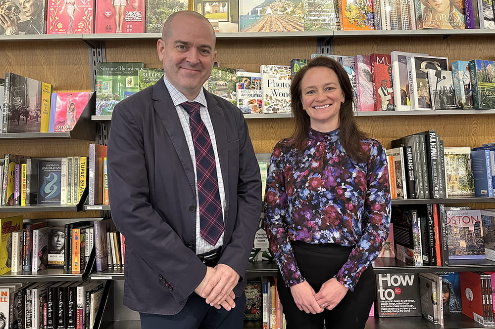 a man and woman pose in front of a wall bookshelf