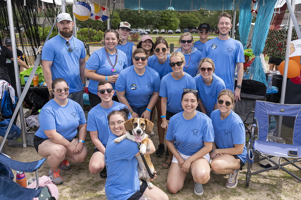 a group of people in blue t-shirts pose for a photo with a dog