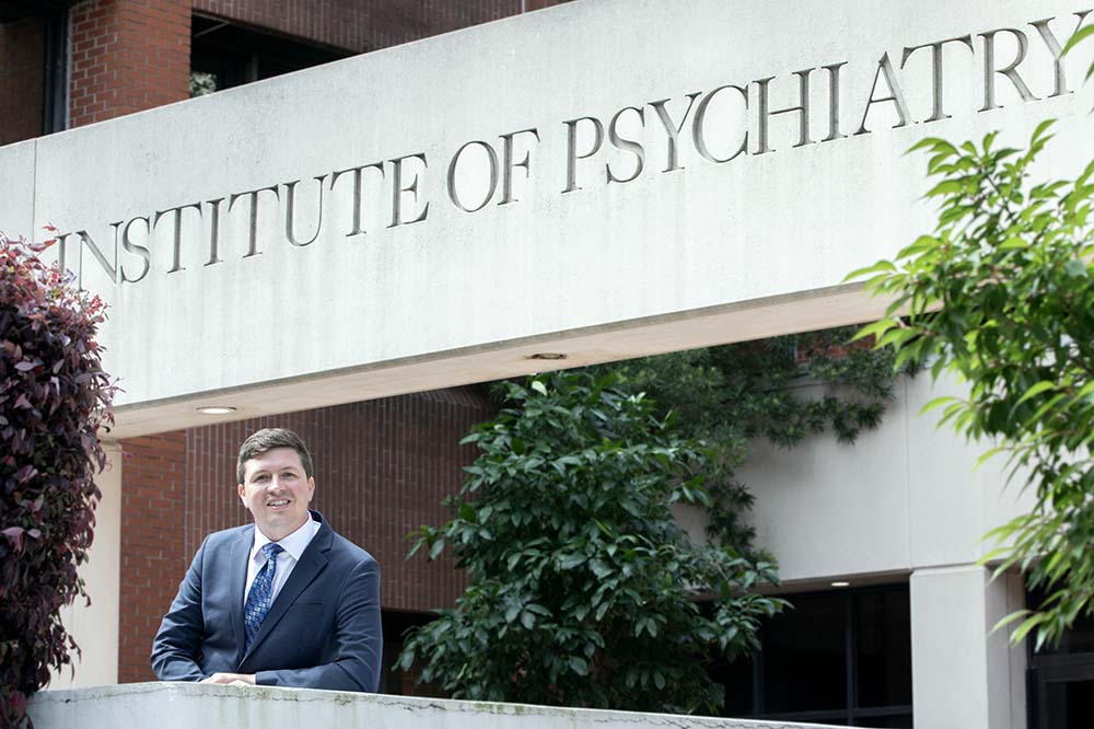 Man in a suit stands below a building sign that says Institute of Psychiatry.