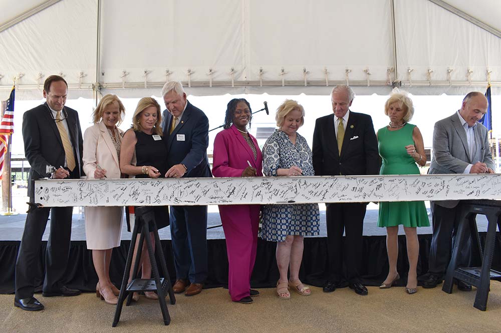 Robby Kerr, Donna Isgett, Kathy Cole, David Cole, Teresa Myers Ervin, Jean Leatherman, Henry McMaster, Peggy McMaster, Patrick Cawley stand behind a beam with signatures on it.