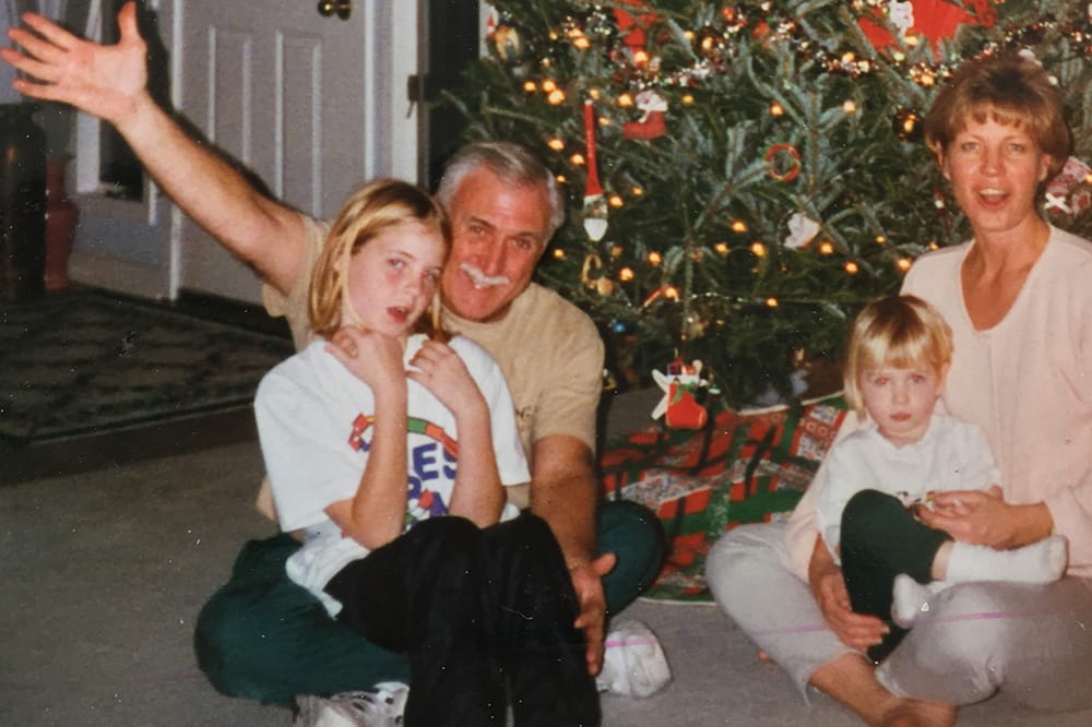 a mom and dad and two young girls sit on the floor in front of a Christmas tree