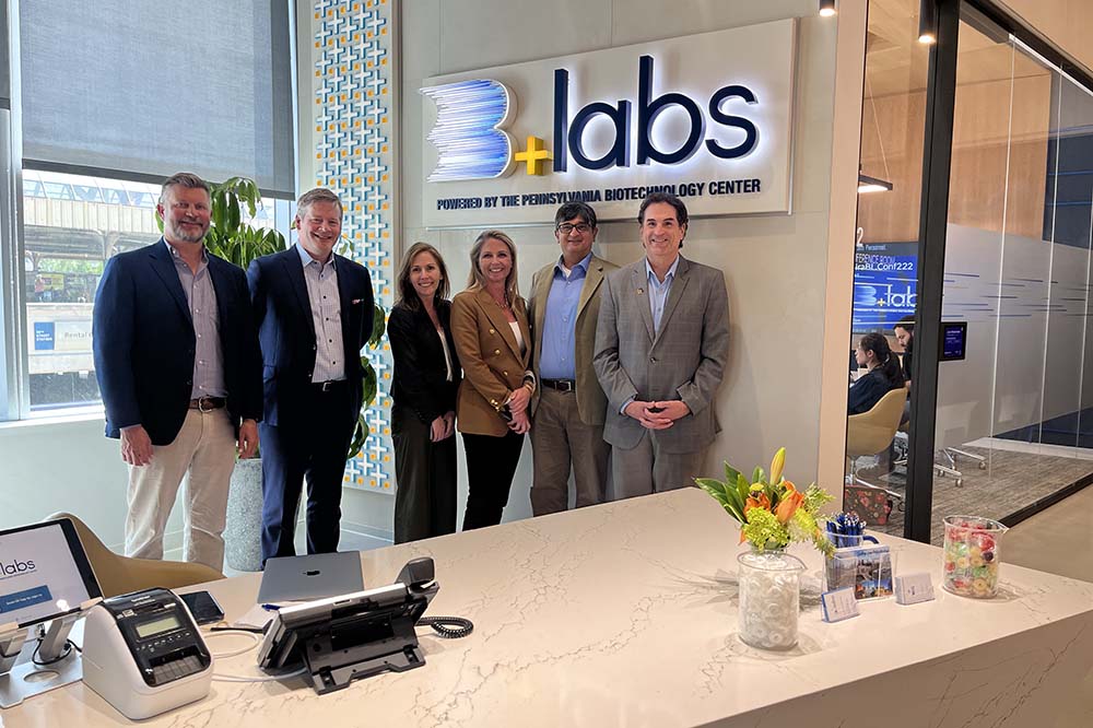 Four men and two women stand under a sign that says B + Labs.