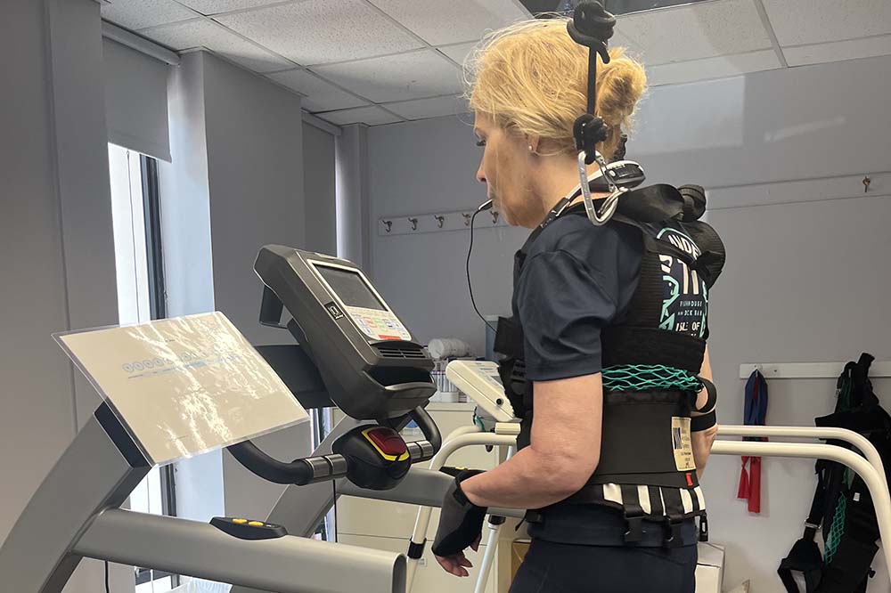 A woman in black workout clothes runs on a treadmill with medical monitoring equipment.