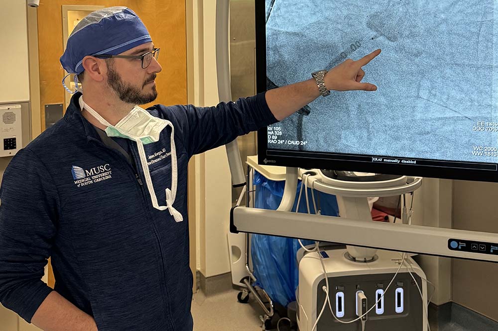 Man in hospital gown points to a screen.