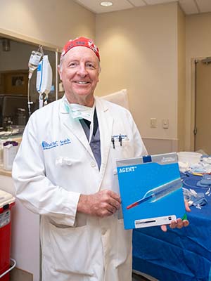 Man in white doctor's coat holds a box that says Agent and has a picture of a medical device.