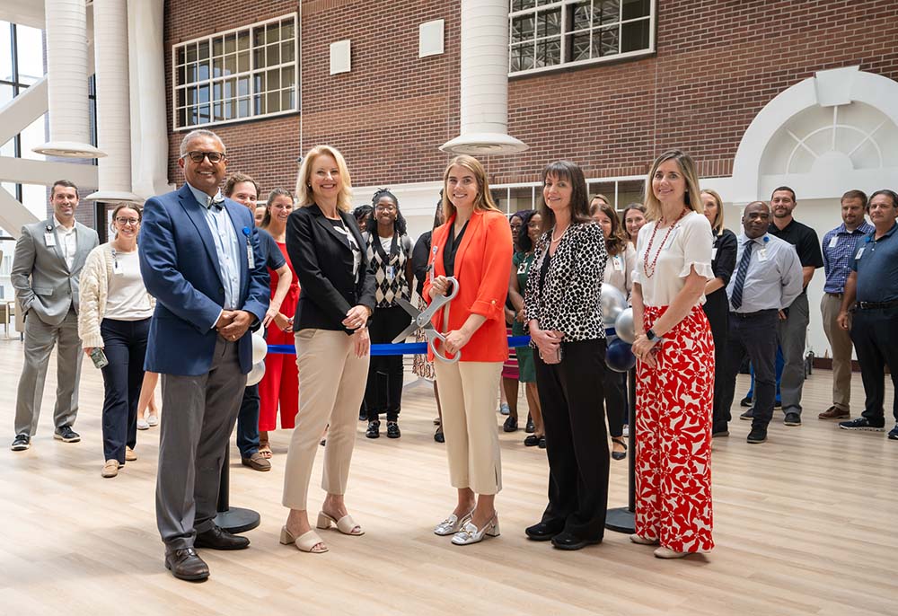 Five people stand by a ribbon they are about to cut.