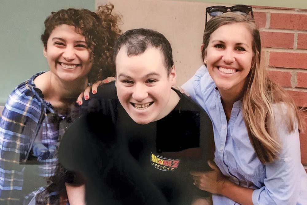 Two women surround a young man who is leaning forward and smiling.