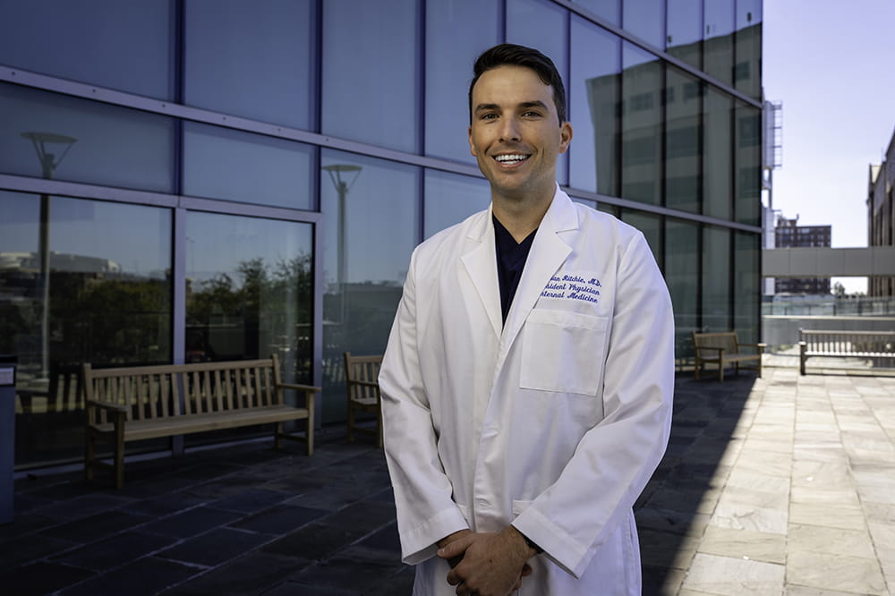 image of young doctor in white coat standing outside a tall glass building