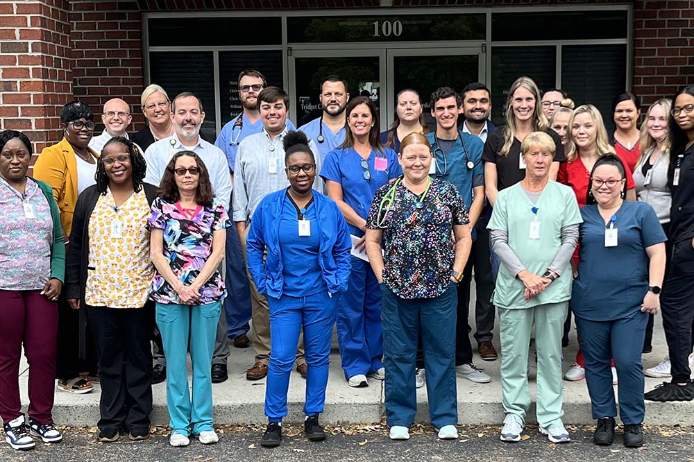 large group of people in hospital scrubs stand in front of brick building.