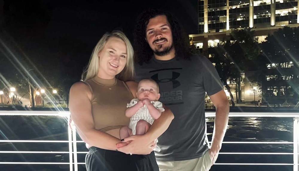 A woman holds a baby with a man standing beside her.