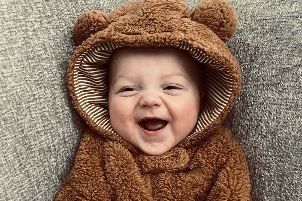 Baby in a bear suit is smiling.