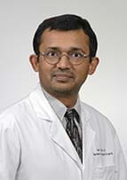 Headshot of smiling man wearing a white doctor's coat and a tie.
