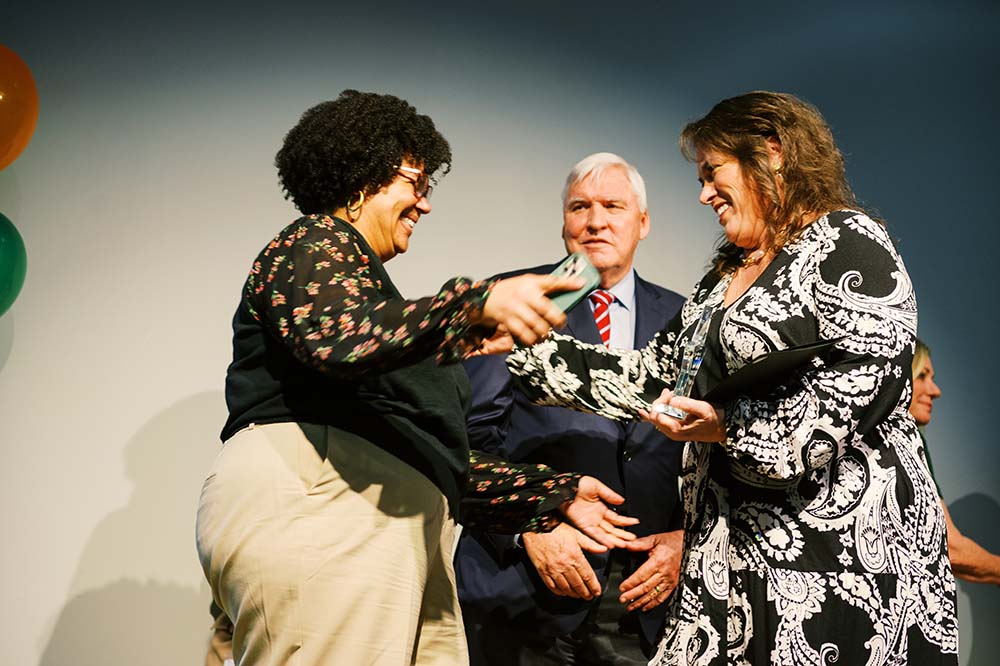 Two women look like they're about to hug. A man standing behind them is smiling.