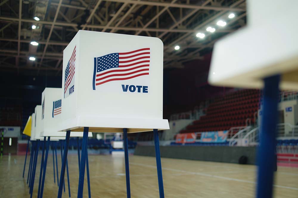 Empty gymnasium with voting booths that have flags on them and the word vote.