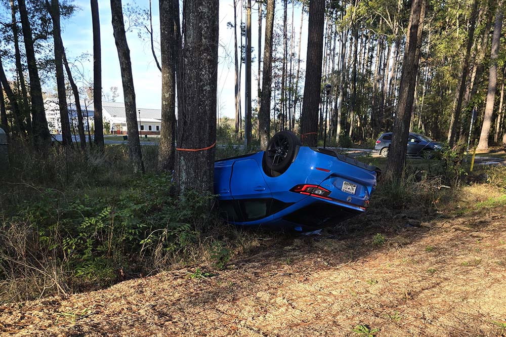 A blue Honda is upside down. It has crashed into a tree.