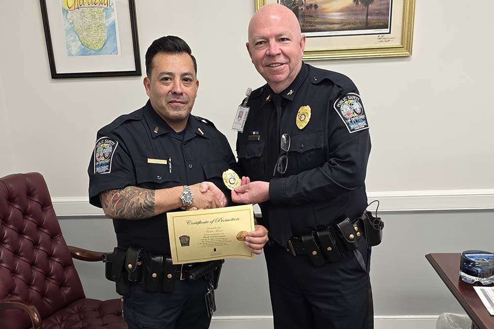 Two policeman in blue uniforms shake hands. They are standing in an office.