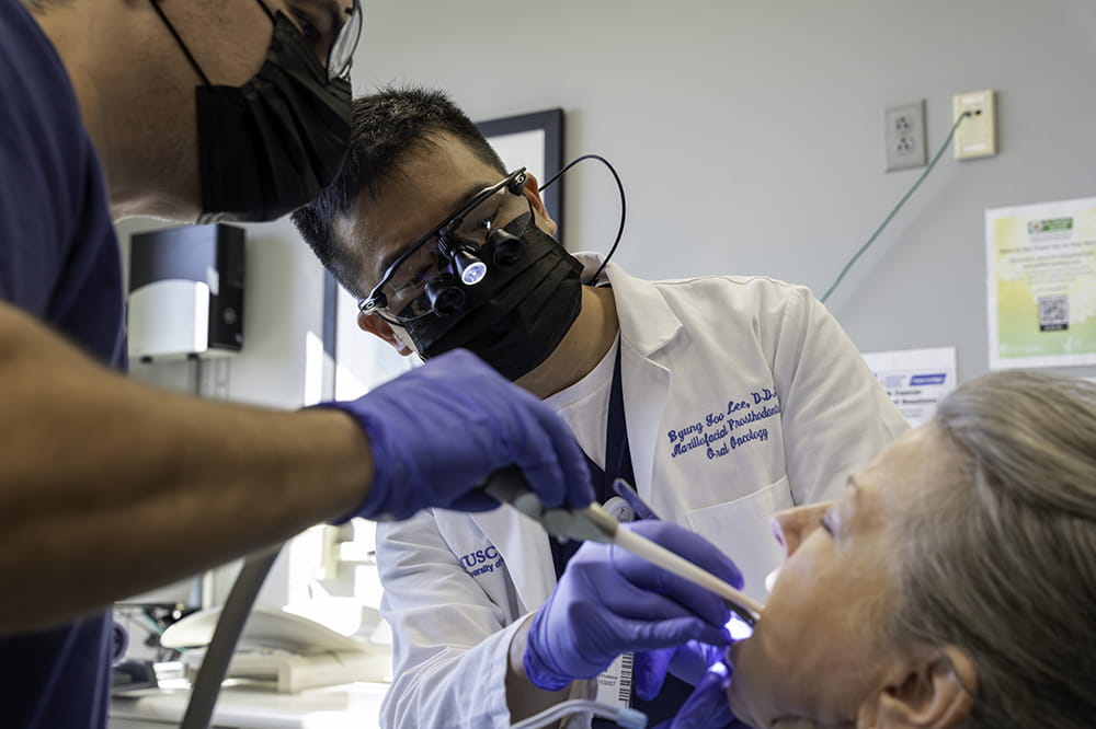 a dentist and assistant examine the inside of a woman's mouth