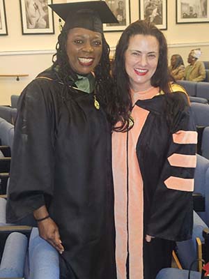 Two women in graduation robes pose in an auditorium.