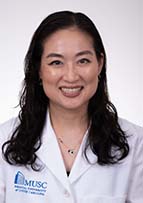 Headshot of woman with long dark hair. She's wearing a white doctor's coat.