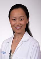 Headshot of a woman with long dark hair wearing a white doctor's coat.