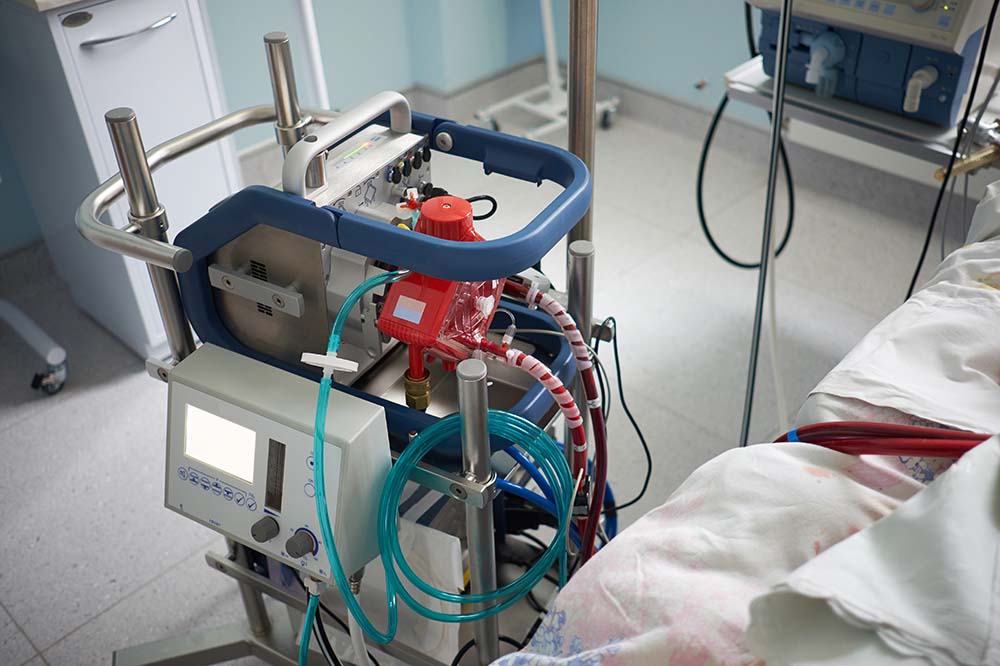 machine with tubes coming out of it next to a hospital bed.