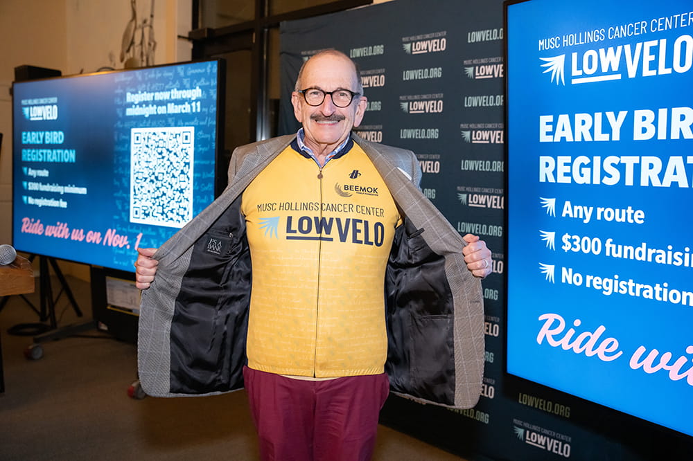 a man holds open his sophisticated blazer to show he's wearing a bright gold cycling jersey