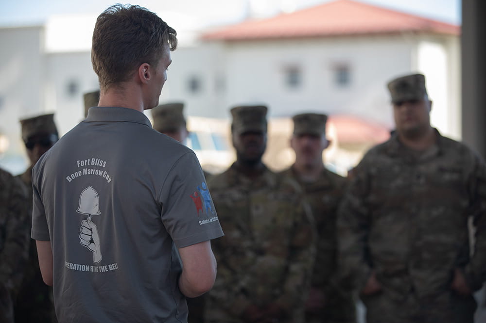 a young man facing away from the camera talks to soldiers in uniform 