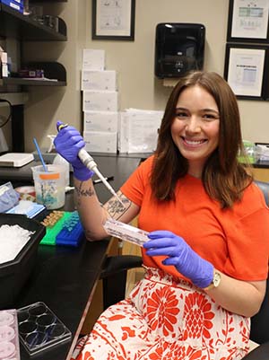 A woman wearing brightly colored clothes smiles while using lab instruments.