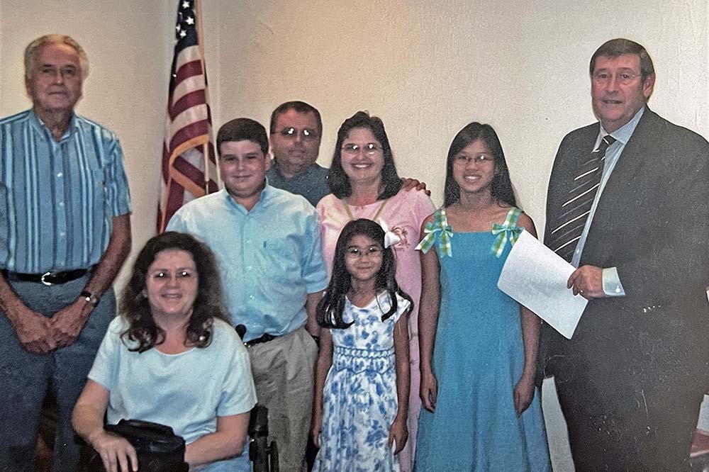 Eight people pose for a portrait with an American flag behind them.