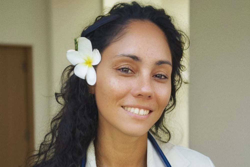 Headshot of woman with curly dark hair and a flower behind her right ear.