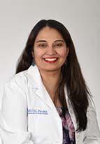Headshot of smiling woman with long dark hair wearing a white coat.