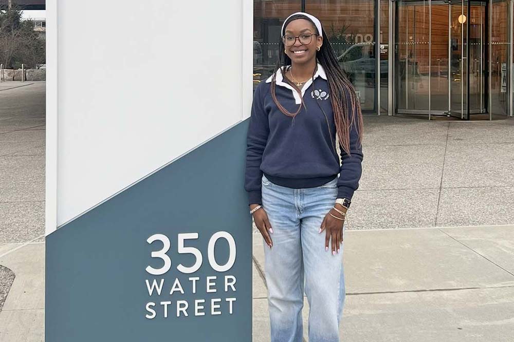 Young woman in long-sleeve top and jeans stands by a sign that says 350 Water Street.
