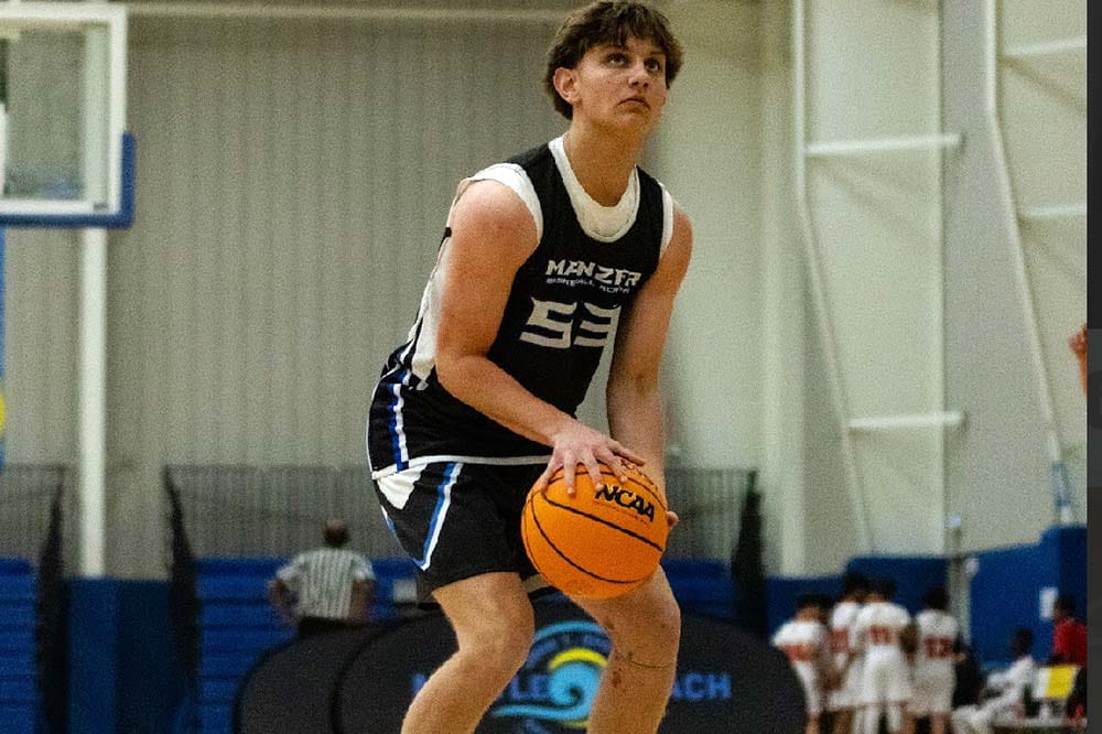 A teenage boy with short dark hair wearing a navy basketball uniform prepares to shoot the ball.