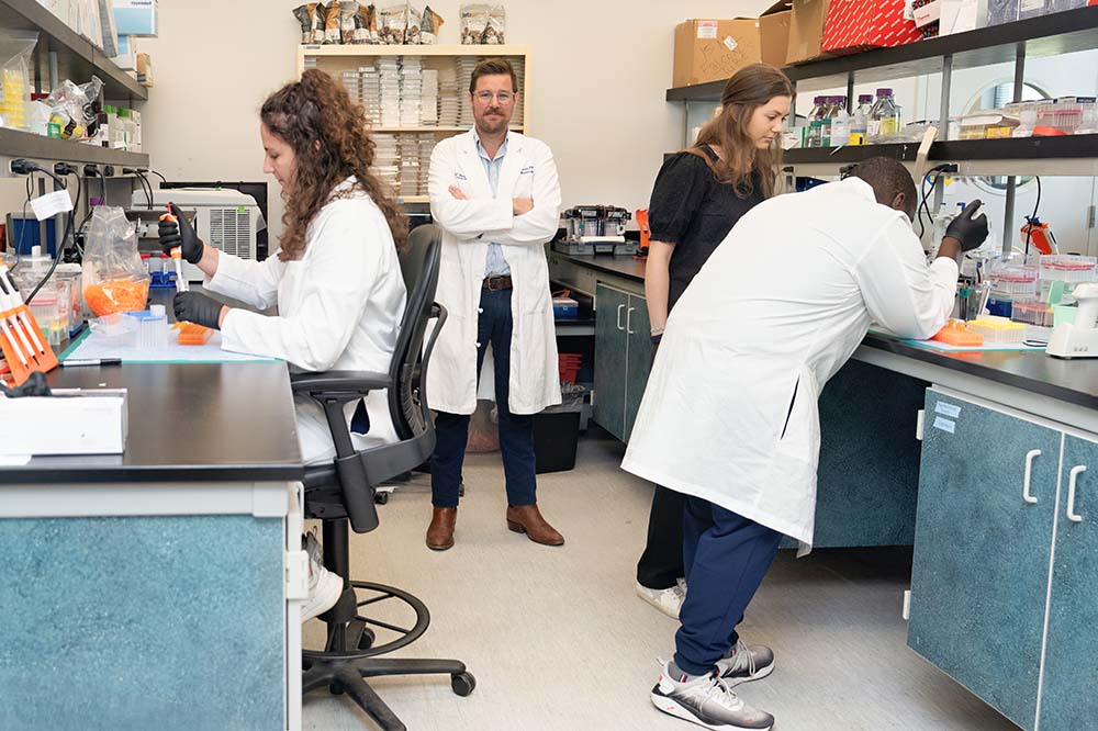 Four people in a laboratory. Three are working, the fourth is standing in the middle.