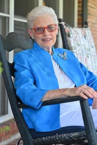 A smiling woman wearing a blue jacket sitting in a chair outside.
