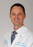 Smiling man with dark hair wearing a white doctor's coat and a necktie.