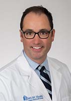 Man with brown hair and glasses wears a white doctor's coat.