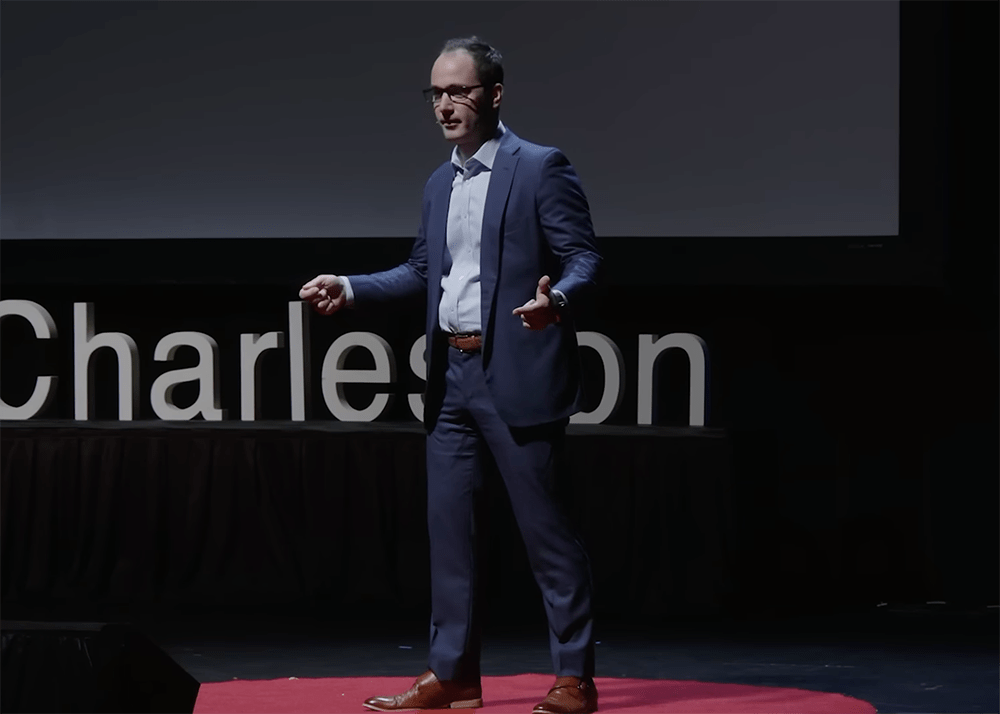 Man in a blue suit gestures while standing on a red platform.