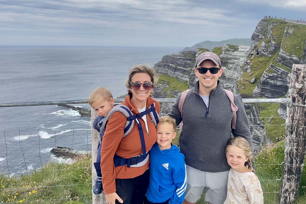 Two adults and three children on a grassy cliff with water behind them.