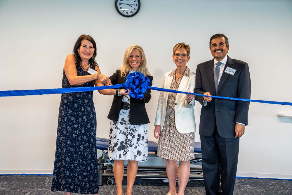 Three women and one man hold a giant blue ribbon.