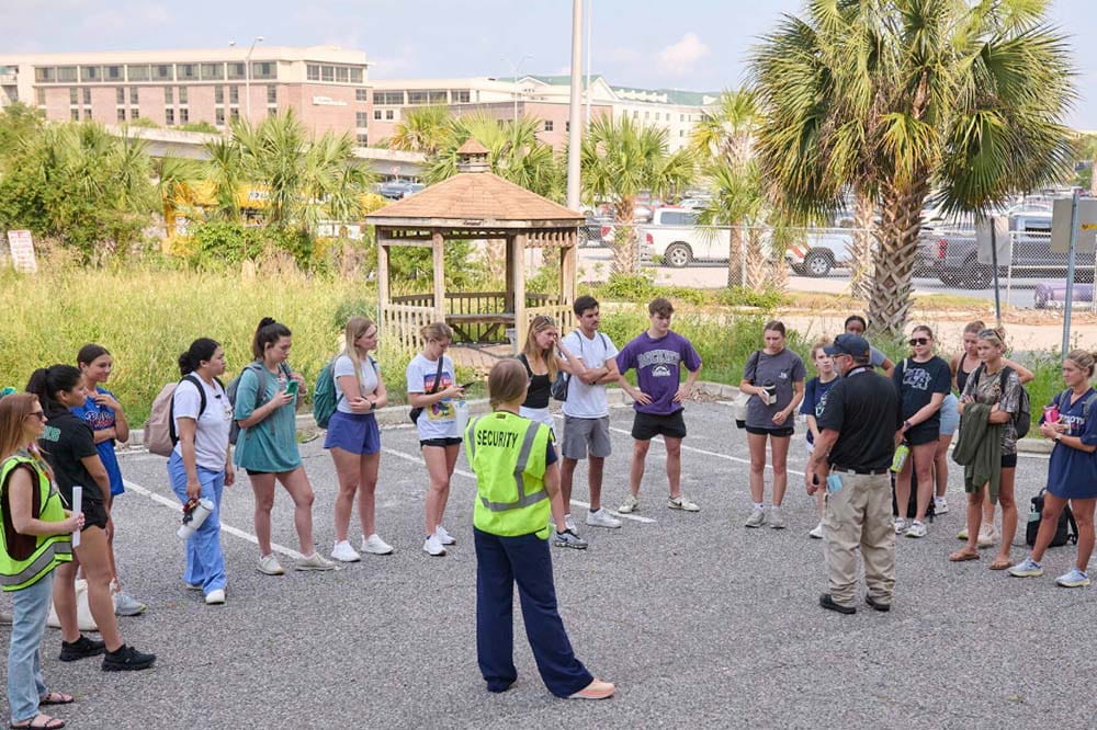 A group of people stand in a semi-circle facing two security officers.