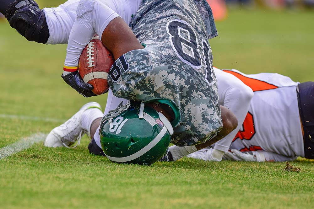 Two football players clash as they hit the ground. The one on top is holding a football.