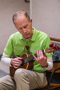 Man is seated, wearing a bright green shirt. He's playing a guitar.