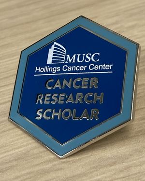 closeup of a lapel pin that says MUSC Hollings Cancer Center Cancer Research Scholar