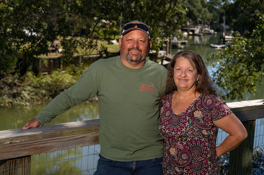 a couple poses along their fence which overlooks a creek behind their house