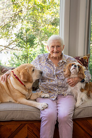a woman poses on her sofa with a large golden Laborador and a spaniel