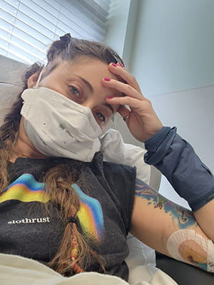 a woman takes a selfie wearing a mask and resting her head on her hand in a medical clinic